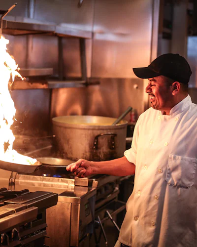 A chef works a flaming pan on a commercial range