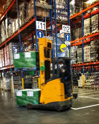 A reach forklift moves pallets in warehouse racking