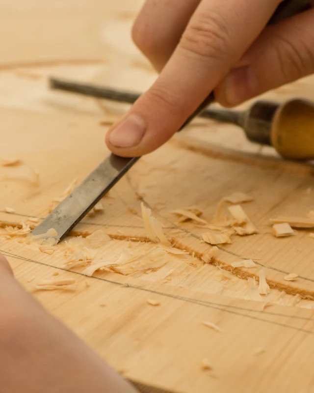 Hands carve wood with a chisel at a workbench